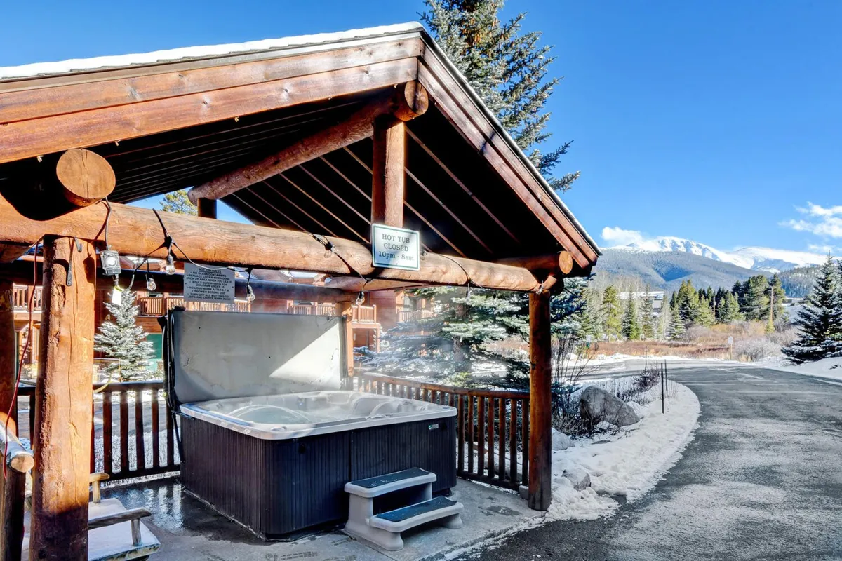 An inviting outdoor hot tub set within a wooden structure, framed by panoramic mountain views. The scene exudes relaxation and social warmth, illustrating the perfect way to unwind after a day of action-packed adventure.