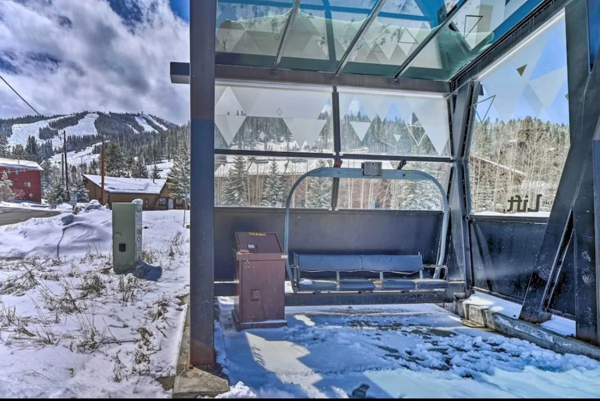 A bustling ski lift surrounded by majestic snow-capped mountains, with a waiting area bench and tracks in the snow indicating recent activity. The image emphasizes the thrill and accessibility of mountain sports right from the property, capturing the excitement of winter recreation.