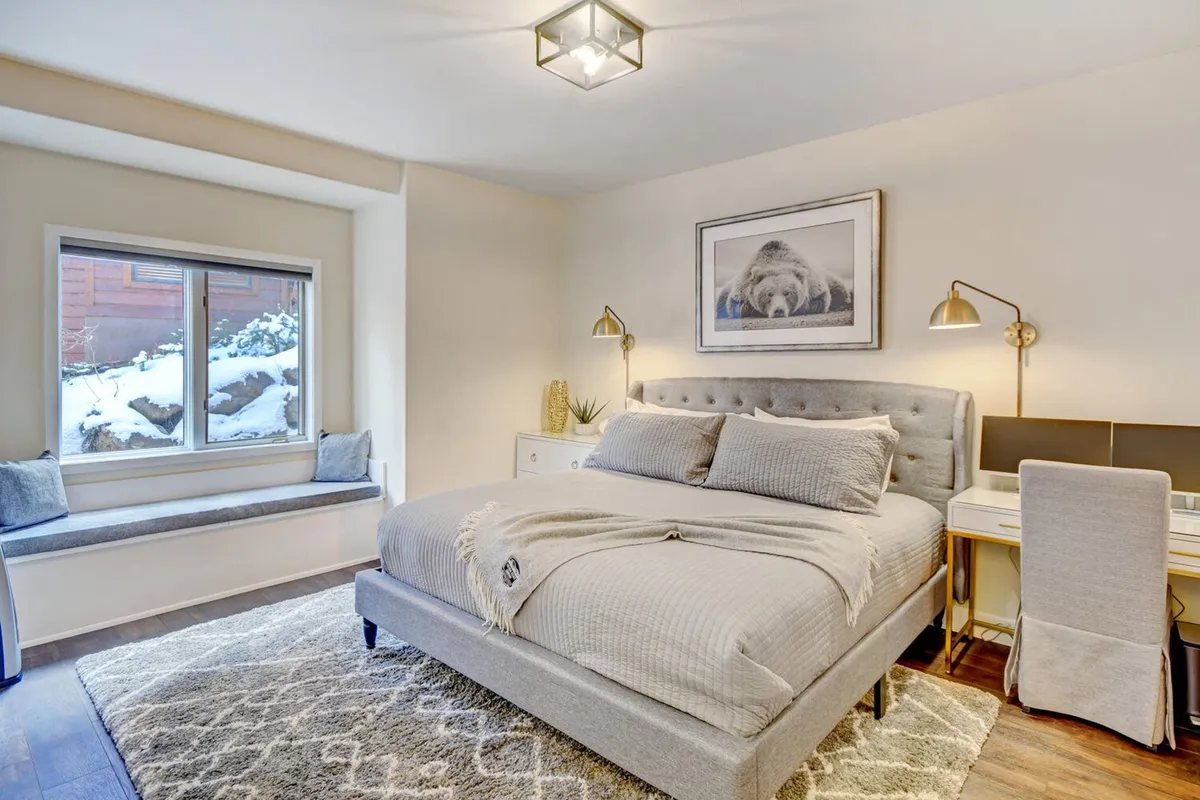 A serene bedroom with a plush bed, window seat, artwork above the headboard, and a dedicated workspace with a desk. Natural light pours in through the window, and a tranquil atmosphere is created by the soft color palette and inviting textures.