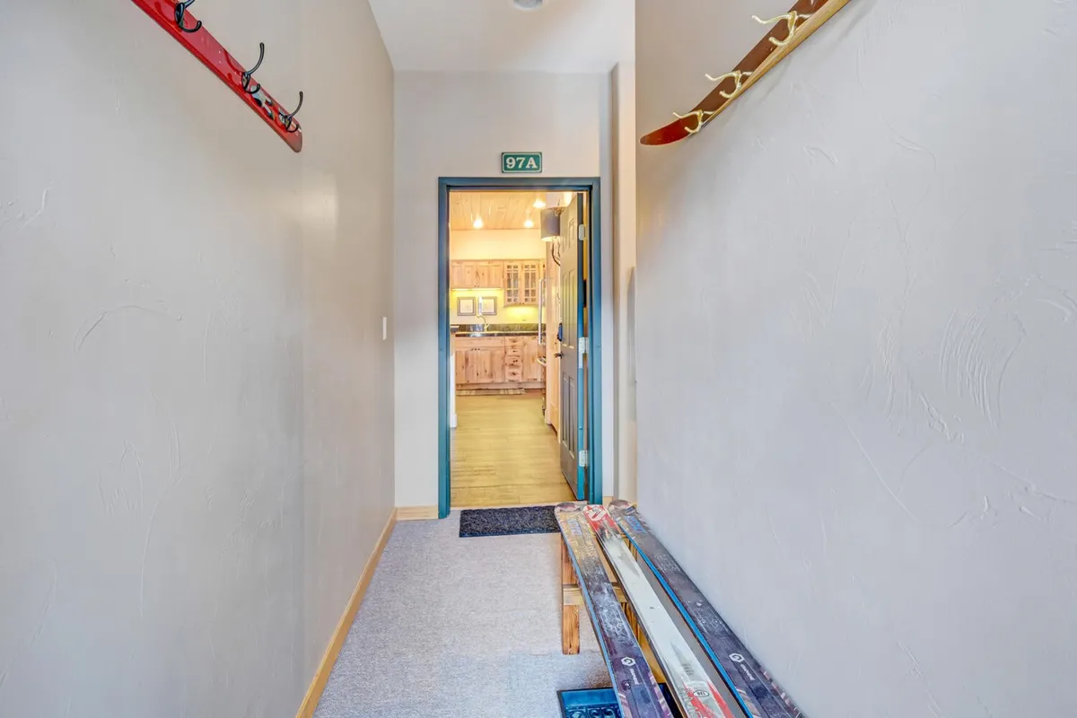 A cozy entryway with coats on hooks, a wooden bench, and a doorway leading to the kitchen. The space is inviting and speaks to the transition from outdoor activities back into the comfort of the condo.
