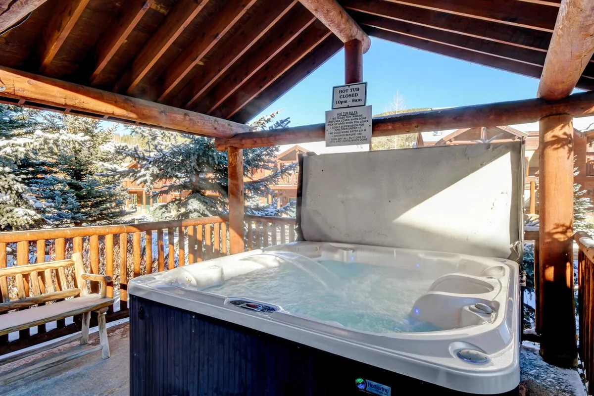 An outdoor hot tub set against a backdrop of tall trees and a rustic wooden railing, offering a tranquil, nature-immersed soaking experience. The area is peaceful and inviting, ideal for post-adventure relaxation.