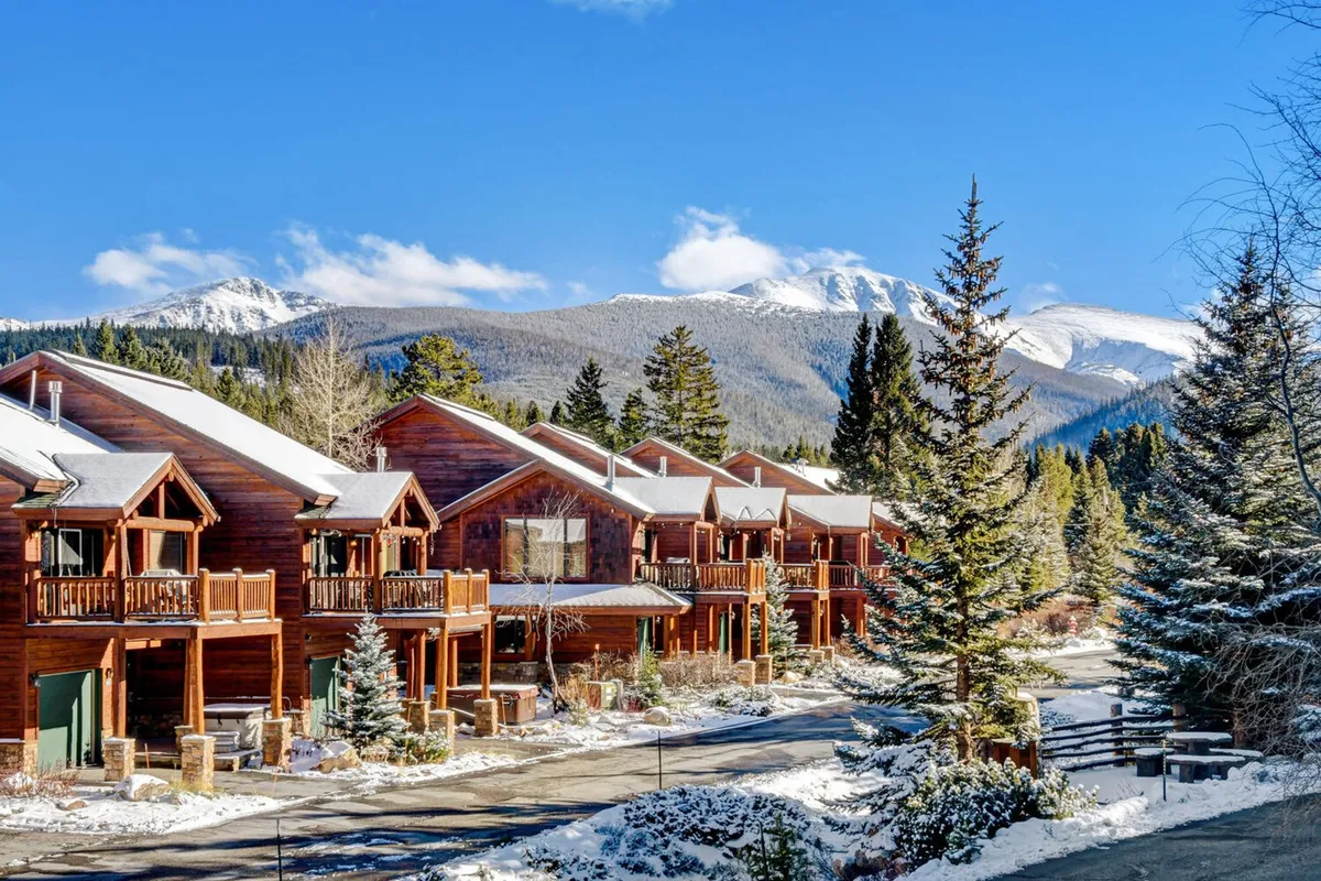 A group of cozy wooden cabins nestled in a snowy landscape, with towering mountains forming a breathtaking backdrop. The scene conveys both tranquility and excitement, hinting at the variety of winter activities available such as skiing, snowboarding, and winter hiking. The cabins evoke comfort and adventure, making it perfect for showcasing the destination's outdoor appeal.