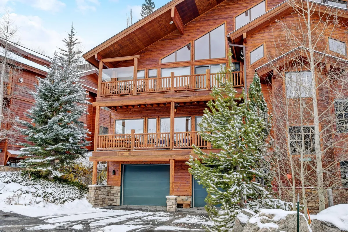 A cozy, snow-covered condominium complex featuring inviting wooden balconies and large windows. The landscape is blanketed in snow, creating a serene winter atmosphere and offering glimpses into the warm, inviting interiors. The scene hints at the comfort and productivity available inside while strongly connecting to the outdoors and mountain setting.