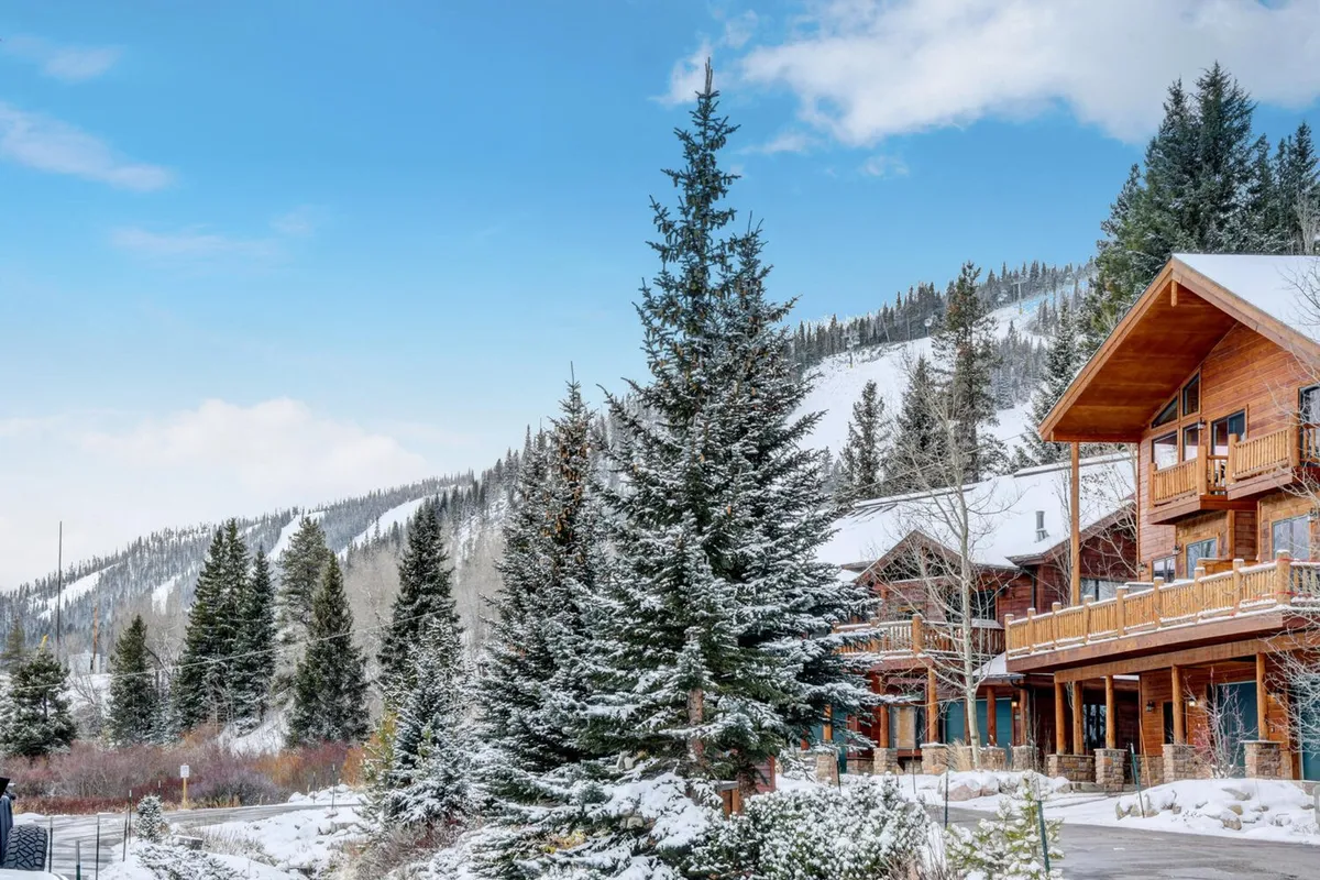 A striking winter mountain scene featuring snow-laden trees, a classic wooden lodge, and a dramatic mountain backdrop. The image exudes tranquility and adventure, inviting guests to enjoy hiking, skiing, or simply soaking in the majestic surroundings right outside the door.
