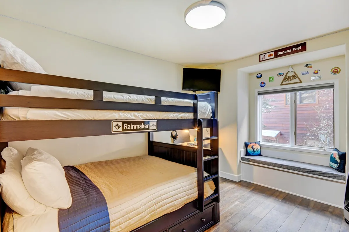 A playful bunkroom featuring bunk beds, window seating, and decorative wall signs. The space has a youthful energy, perfect for kids or anyone young at heart, with cozy beds and an inviting nook by the window.