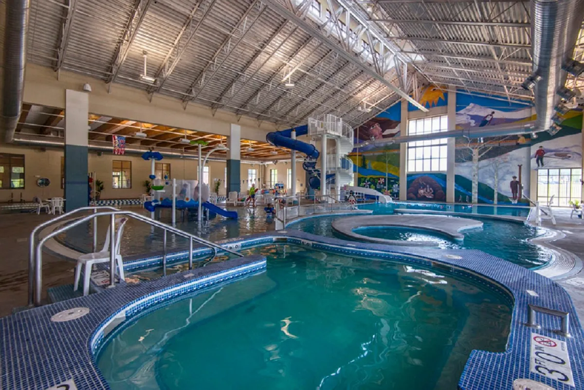 A vibrant swimming pool area featuring water slides, playful decorative murals, and families gathered together, radiating energy and fun.