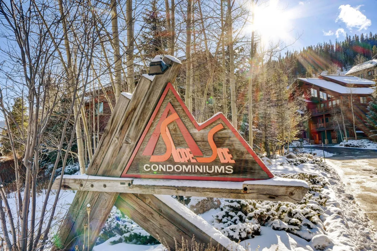 A scenic exterior of the Slope Side Condominiums sign set amidst a snow-covered landscape and surrounded by trees. The image hints at outdoor recreational opportunities and the cozy, inviting atmosphere of the property.