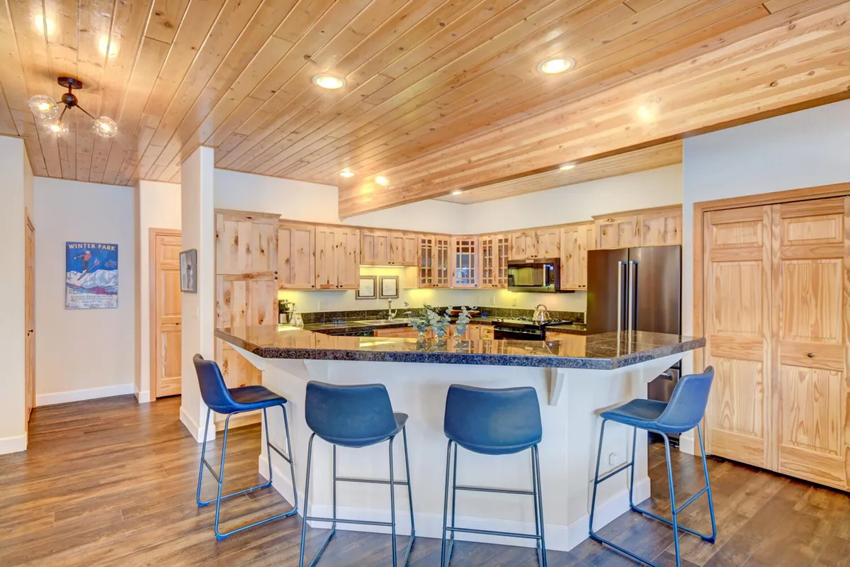 A warmly appointed kitchen with a granite island, rich wooden cabinets, and bar stools offering a casual place for dining or conversation. Soft lighting and decorative touches create a cozy, inviting mood, ideal for both morning coffee and celebratory dinners.